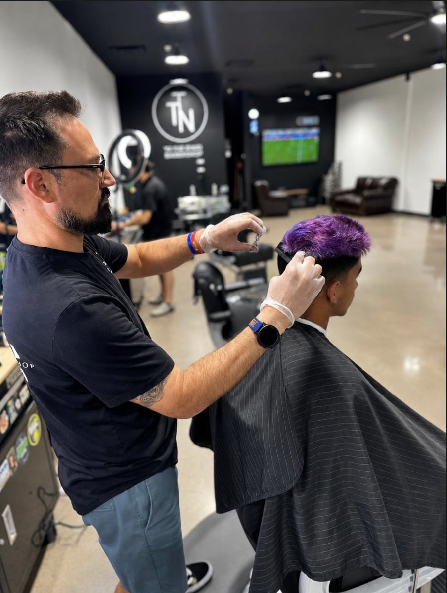 Barber cutting a purple-colored fade at To the Nines Barbershop